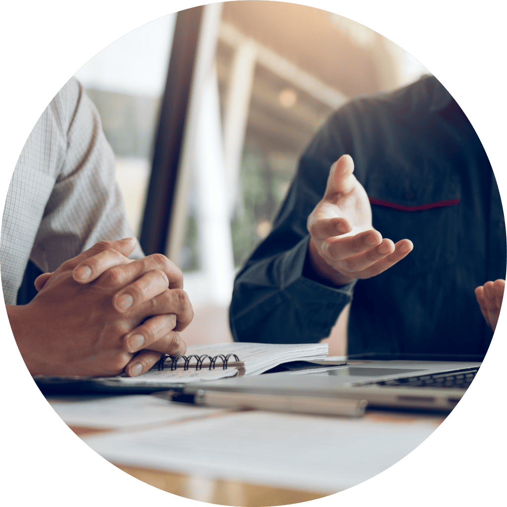 Two financial advisors talking with a client. Photo shows to men at a desk with lap top and paperwork.